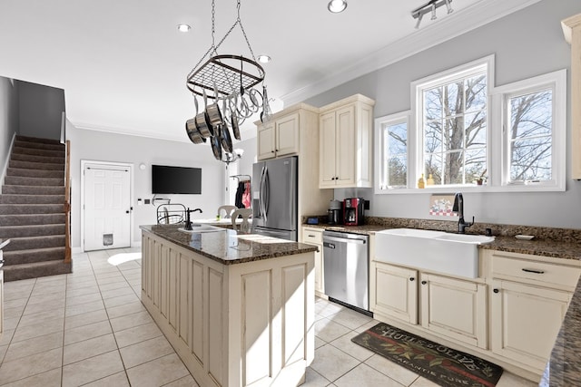 kitchen with sink, ornamental molding, an island with sink, stainless steel appliances, and cream cabinetry