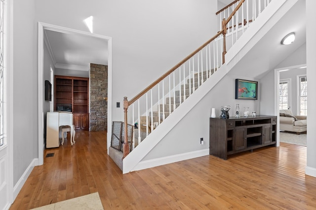 staircase featuring a towering ceiling, wood-type flooring, and ornamental molding