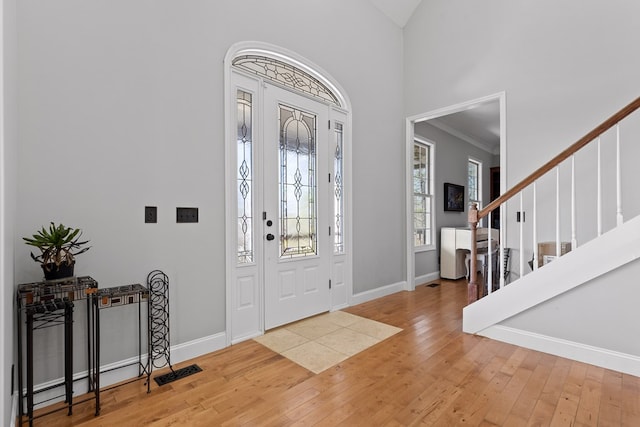 entrance foyer with crown molding, a towering ceiling, and hardwood / wood-style floors