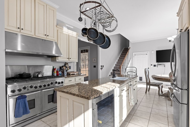 kitchen with appliances with stainless steel finishes, beverage cooler, a center island with sink, cream cabinetry, and dark stone counters