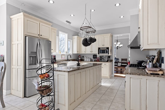 kitchen featuring wall chimney range hood, light tile patterned floors, stainless steel appliances, cream cabinets, and an island with sink