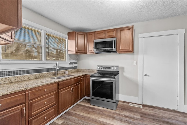 kitchen featuring sink, stainless steel appliances, light hardwood / wood-style floors, light stone countertops, and a textured ceiling