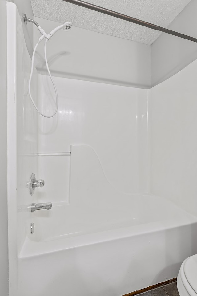 bathroom with shower / bathing tub combination, toilet, and a textured ceiling