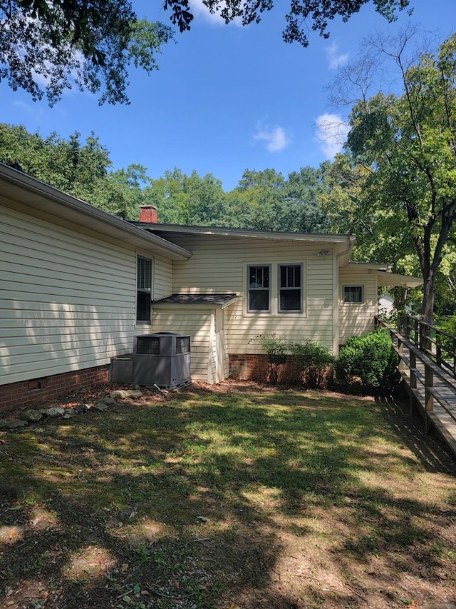 rear view of property with central air condition unit and a lawn