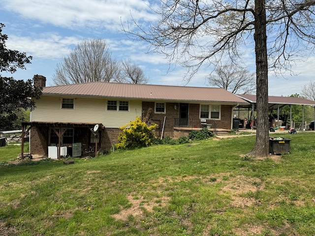 rear view of property with metal roof, brick siding, a yard, and a chimney