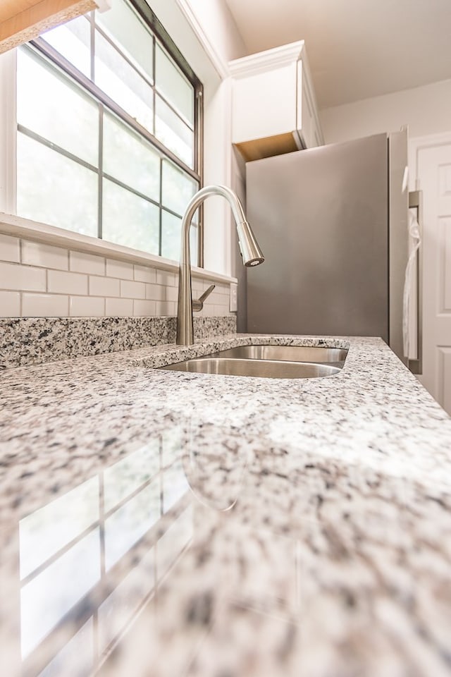 kitchen with white cabinets, tasteful backsplash, freestanding refrigerator, and a sink