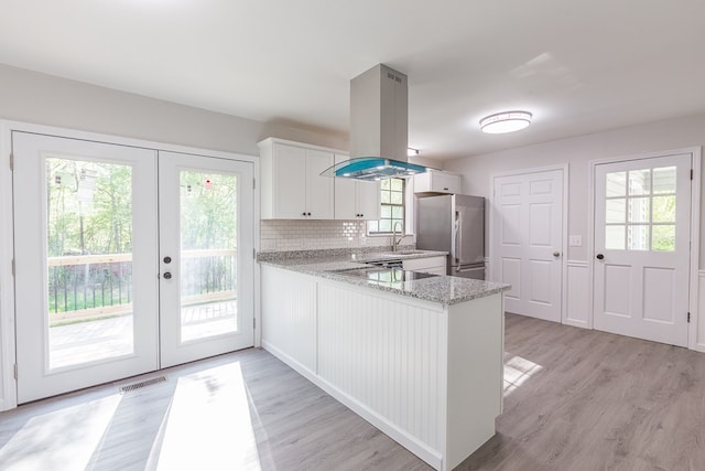 kitchen with freestanding refrigerator, a sink, french doors, white cabinetry, and island range hood