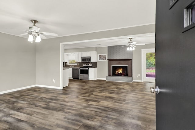 unfurnished living room featuring a brick fireplace, dark wood-type flooring, and ceiling fan