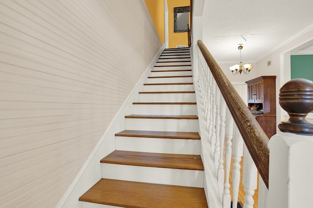 staircase featuring crown molding, a textured ceiling, and a chandelier