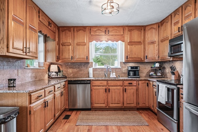 kitchen with stainless steel appliances, light wood-style flooring, a sink, and brown cabinets