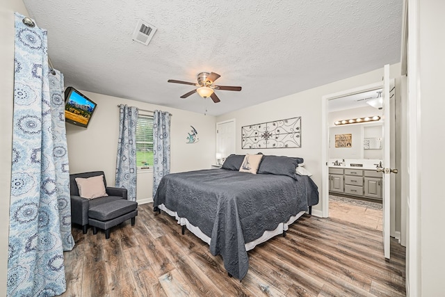 bedroom with a ceiling fan, wood finished floors, ensuite bathroom, baseboards, and visible vents