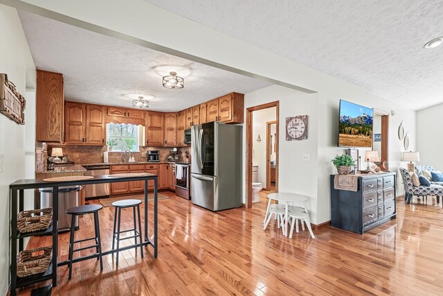 kitchen featuring brown cabinets, light wood-type flooring, a textured ceiling, and stainless steel appliances
