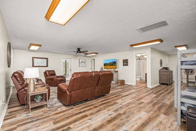 living room with a textured ceiling, baseboards, visible vents, wood finished floors, and ceiling fan
