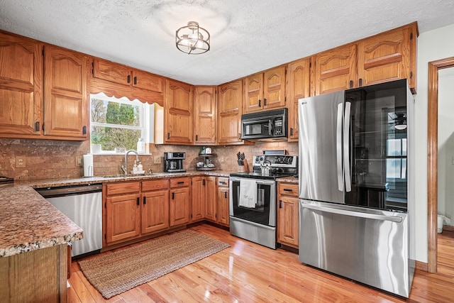 kitchen featuring brown cabinets, appliances with stainless steel finishes, a sink, and light wood finished floors