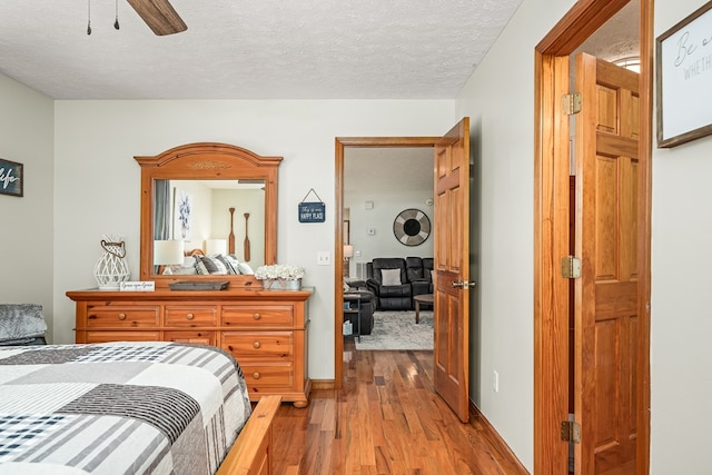 bedroom featuring wood finished floors, a textured ceiling, baseboards, and ceiling fan