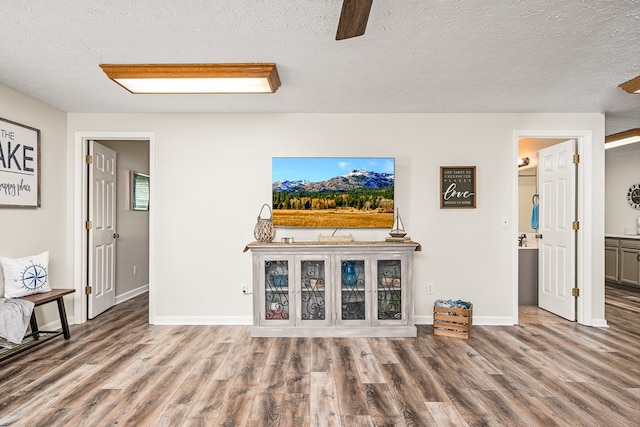 unfurnished living room featuring ceiling fan, baseboards, wood finished floors, and a textured ceiling