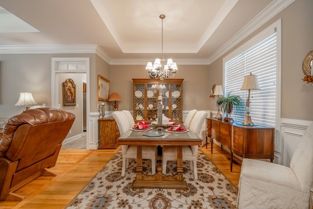 dining space featuring light wood-style flooring, a tray ceiling, an inviting chandelier, and a wainscoted wall
