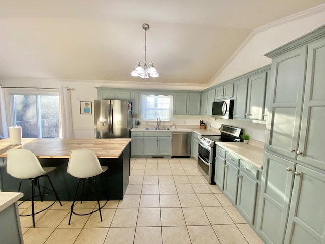 kitchen featuring light tile patterned flooring, lofted ceiling, sink, hanging light fixtures, and stainless steel appliances