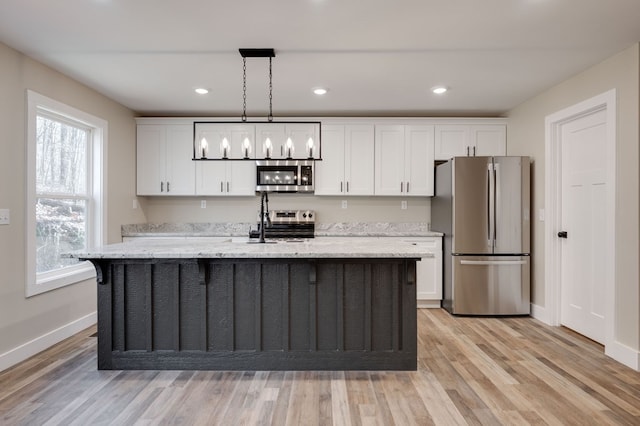 kitchen featuring stainless steel appliances, decorative light fixtures, an island with sink, and white cabinets