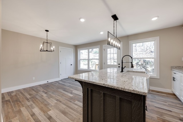 kitchen featuring sink, a kitchen island with sink, light stone counters, a wealth of natural light, and white cabinets