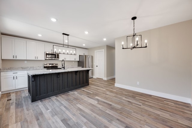 kitchen featuring appliances with stainless steel finishes, a kitchen island with sink, light hardwood / wood-style floors, white cabinets, and decorative light fixtures