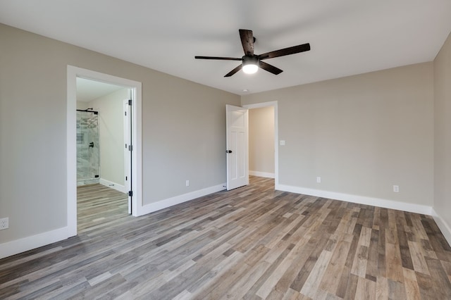 unfurnished bedroom with light hardwood / wood-style floors, a barn door, ceiling fan, and ensuite bathroom