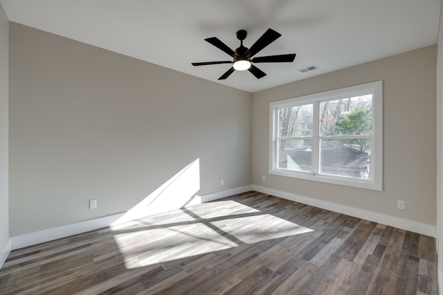 empty room with dark wood-type flooring, a ceiling fan, visible vents, and baseboards