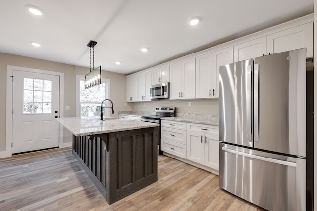 kitchen with stainless steel appliances, a center island with sink, white cabinetry, and light stone countertops