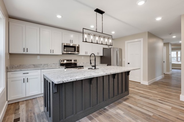 kitchen with pendant lighting, stainless steel appliances, an island with sink, and white cabinets