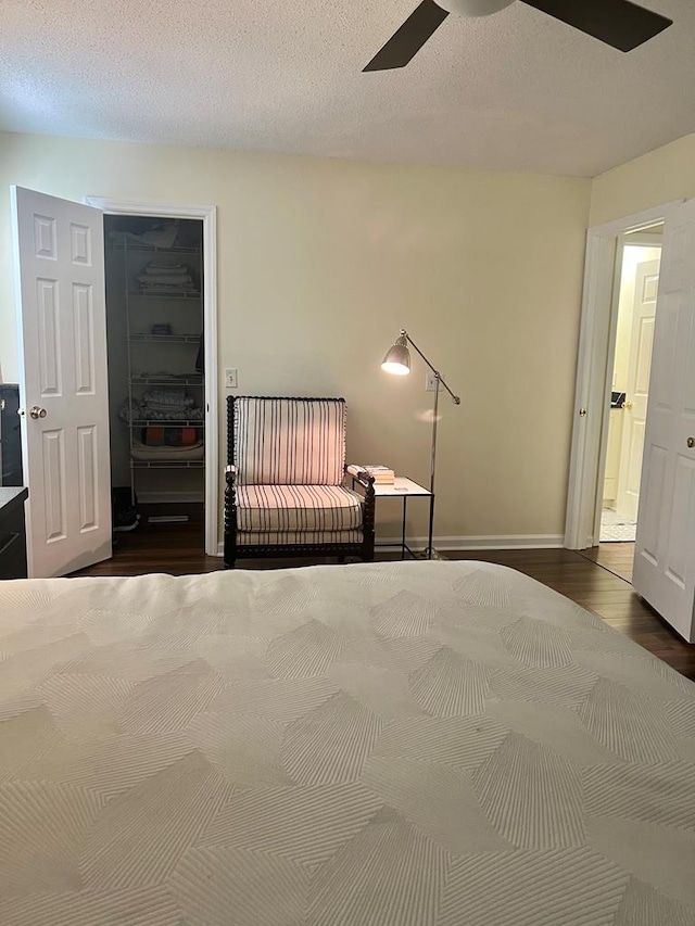 unfurnished bedroom featuring ceiling fan, a textured ceiling, dark hardwood / wood-style flooring, a spacious closet, and a closet