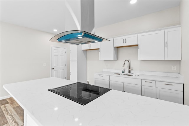 kitchen featuring light stone countertops, stovetop, island exhaust hood, a sink, and white cabinets