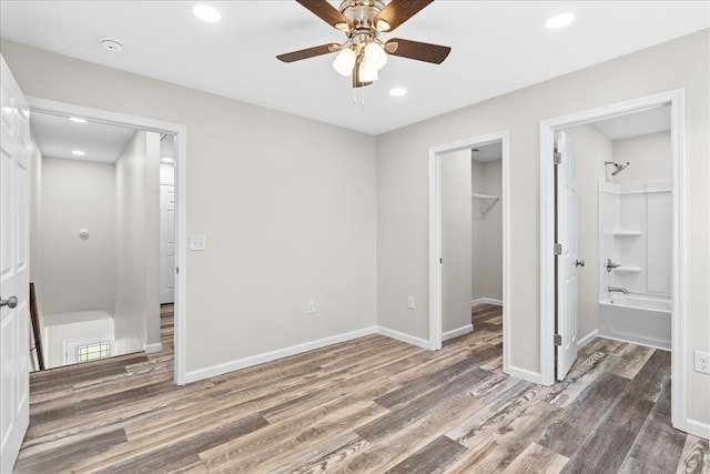 unfurnished bedroom featuring a walk in closet, baseboards, recessed lighting, wood finished floors, and a closet