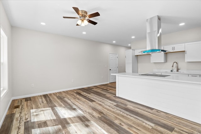 kitchen with island exhaust hood, a sink, wood finished floors, white cabinetry, and light countertops