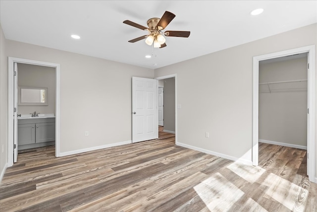 unfurnished bedroom with a sink, a walk in closet, baseboards, and light wood-style floors