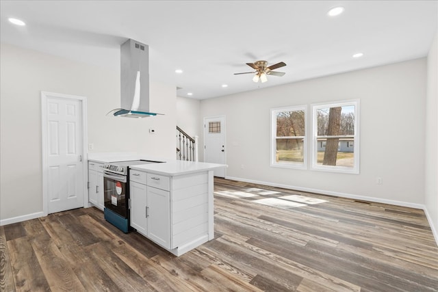 kitchen with wood finished floors, a peninsula, electric range, ceiling fan, and wall chimney range hood