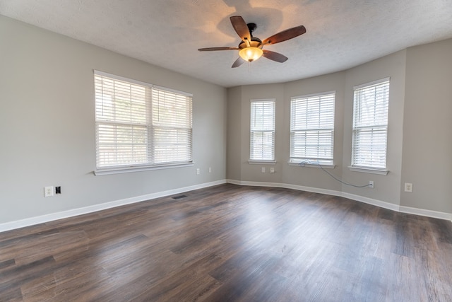 empty room featuring ceiling fan, a wealth of natural light, dark hardwood / wood-style floors, and a textured ceiling