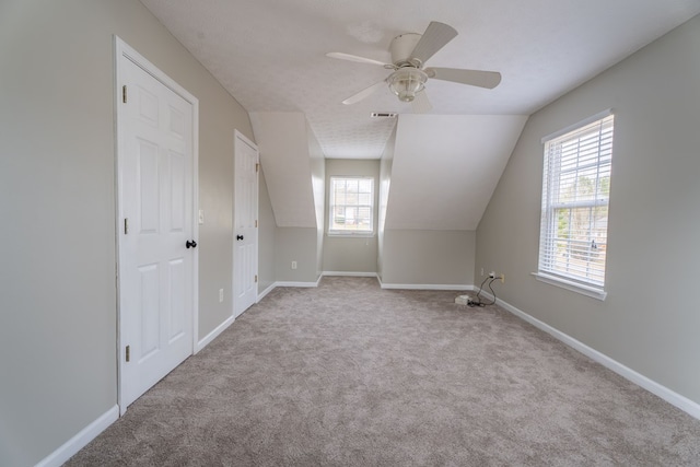 additional living space with ceiling fan, vaulted ceiling, light carpet, and a textured ceiling