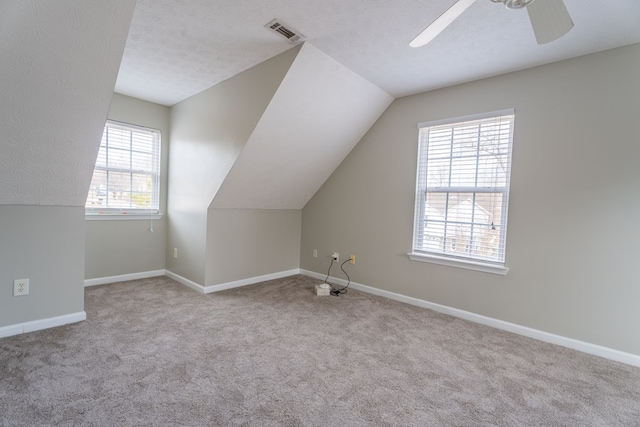 additional living space featuring lofted ceiling, ceiling fan, light colored carpet, and a textured ceiling