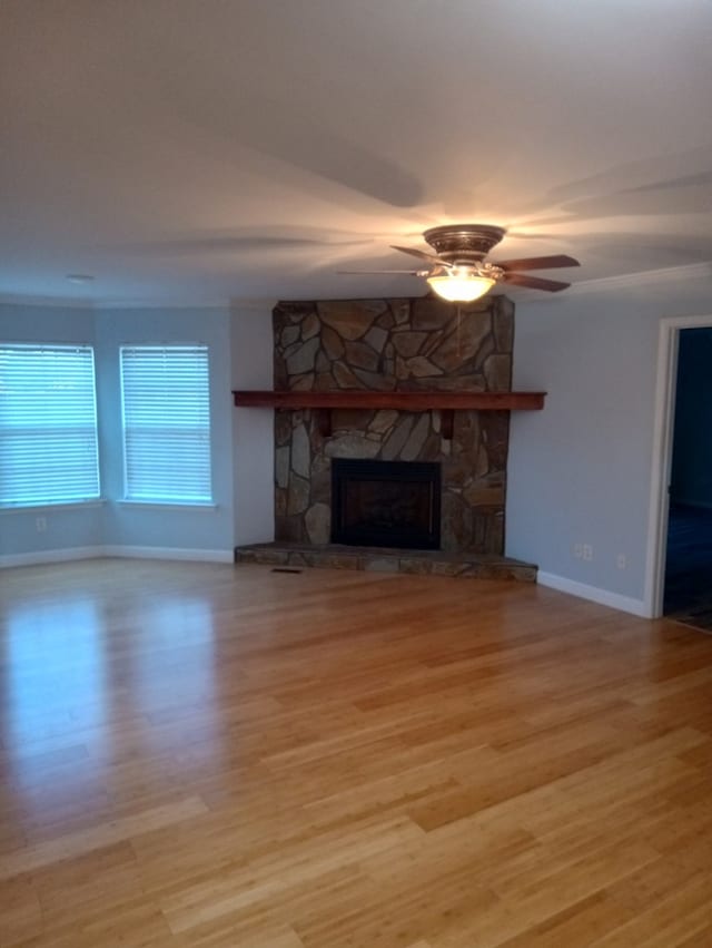 unfurnished living room featuring a stone fireplace, ornamental molding, light hardwood / wood-style floors, and ceiling fan