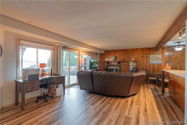 living room with a textured ceiling, wood walls, ceiling fan, and light hardwood / wood-style floors