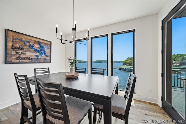 dining area with a water view, light wood-type flooring, plenty of natural light, and a chandelier