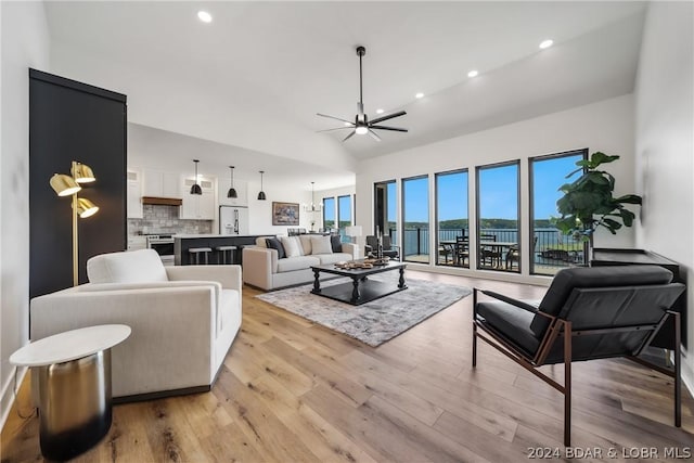 living room featuring ceiling fan with notable chandelier, light wood-type flooring, and lofted ceiling