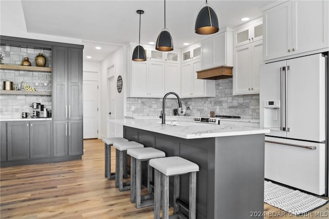 kitchen featuring high end white refrigerator, light stone counters, decorative backsplash, white cabinets, and decorative light fixtures