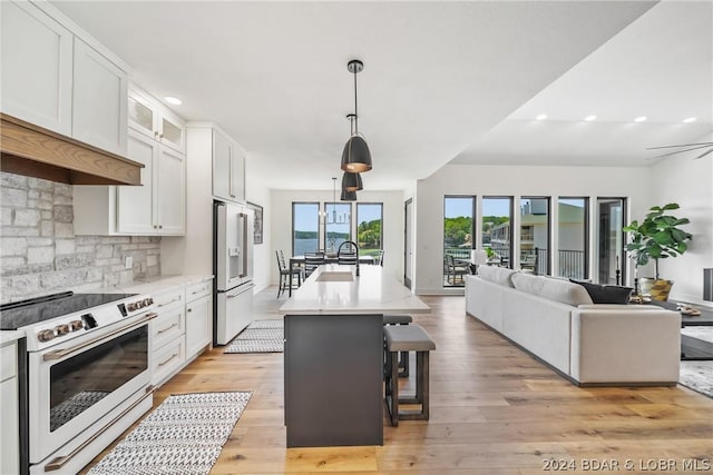 kitchen featuring white appliances, a kitchen island with sink, a kitchen bar, white cabinets, and decorative light fixtures