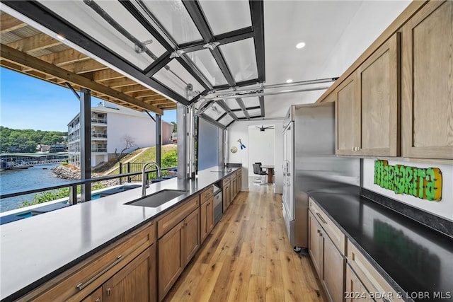 kitchen with sink, a water view, ceiling fan, light hardwood / wood-style floors, and stainless steel fridge