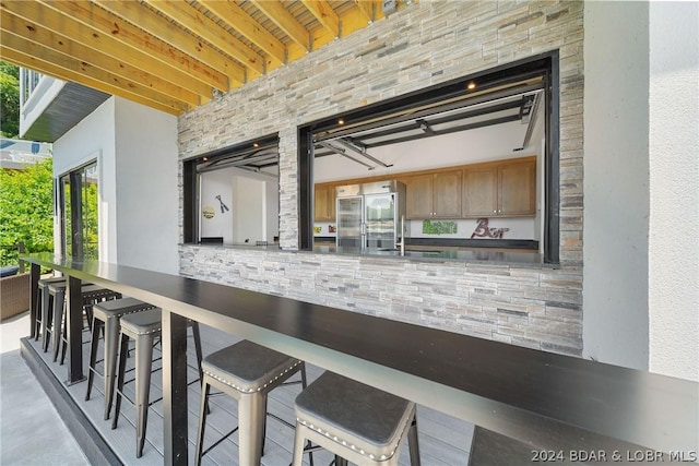 kitchen featuring sink, stainless steel built in refrigerator, beamed ceiling, and a kitchen bar