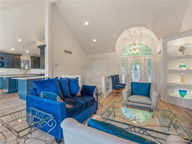 living room featuring light hardwood / wood-style flooring, built in shelves, high vaulted ceiling, and an inviting chandelier