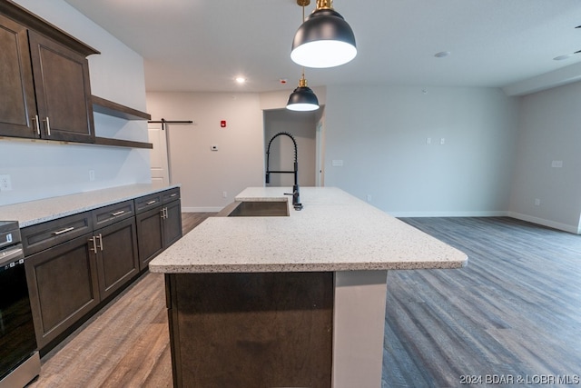 kitchen with hanging light fixtures, a kitchen island with sink, a barn door, wood-type flooring, and sink