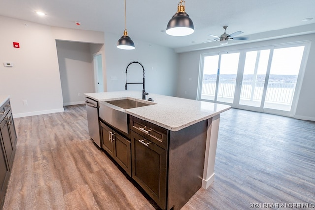 kitchen with sink, light hardwood / wood-style floors, decorative light fixtures, stainless steel dishwasher, and light stone counters