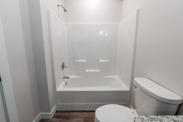 bathroom with washtub / shower combination, hardwood / wood-style flooring, and toilet